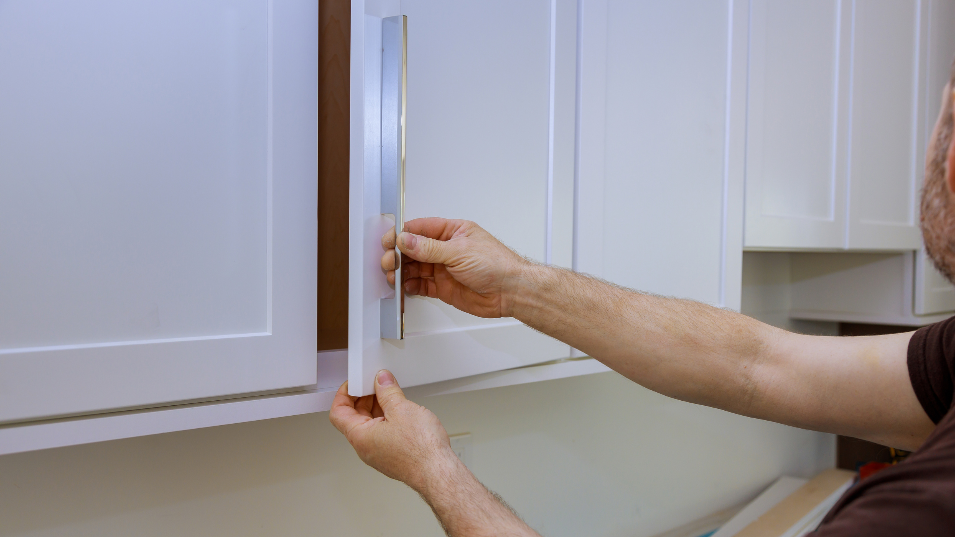 A man is opening a cabinet door in a kitchen.