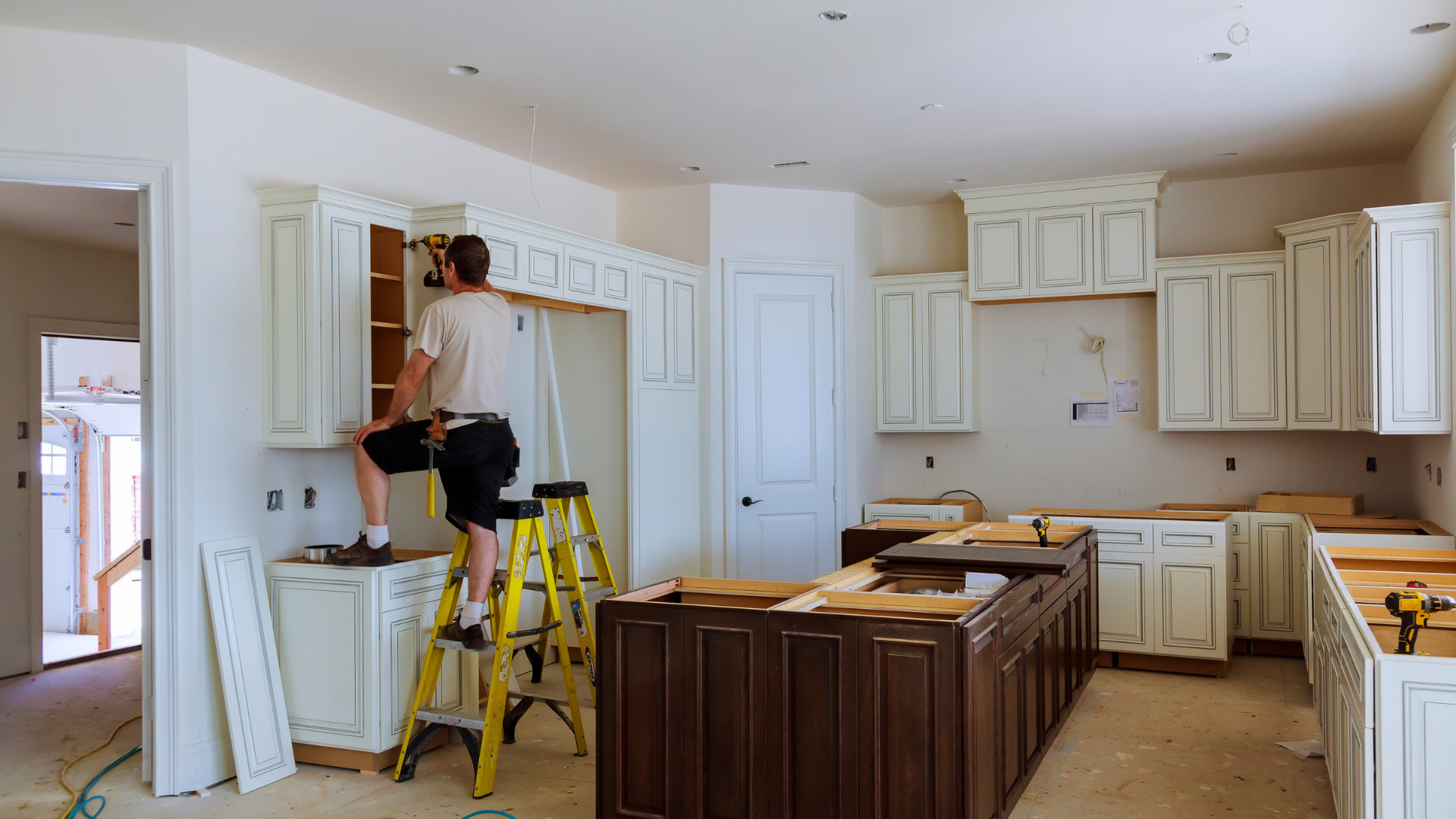 A man is standing on a ladder in a kitchen under construction.