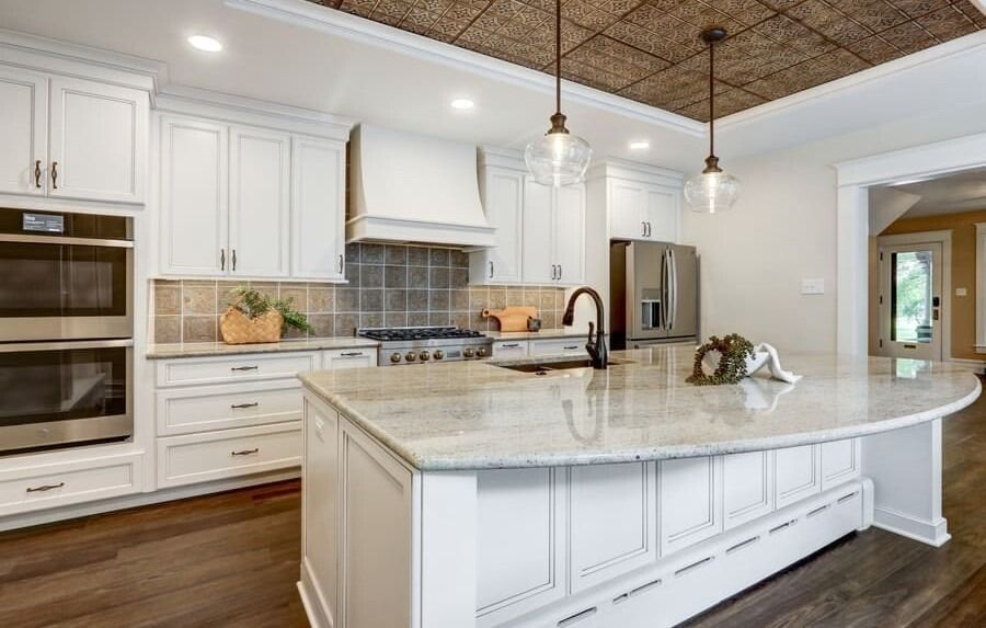 A kitchen with white cabinets , granite counter tops , stainless steel appliances and a large island.