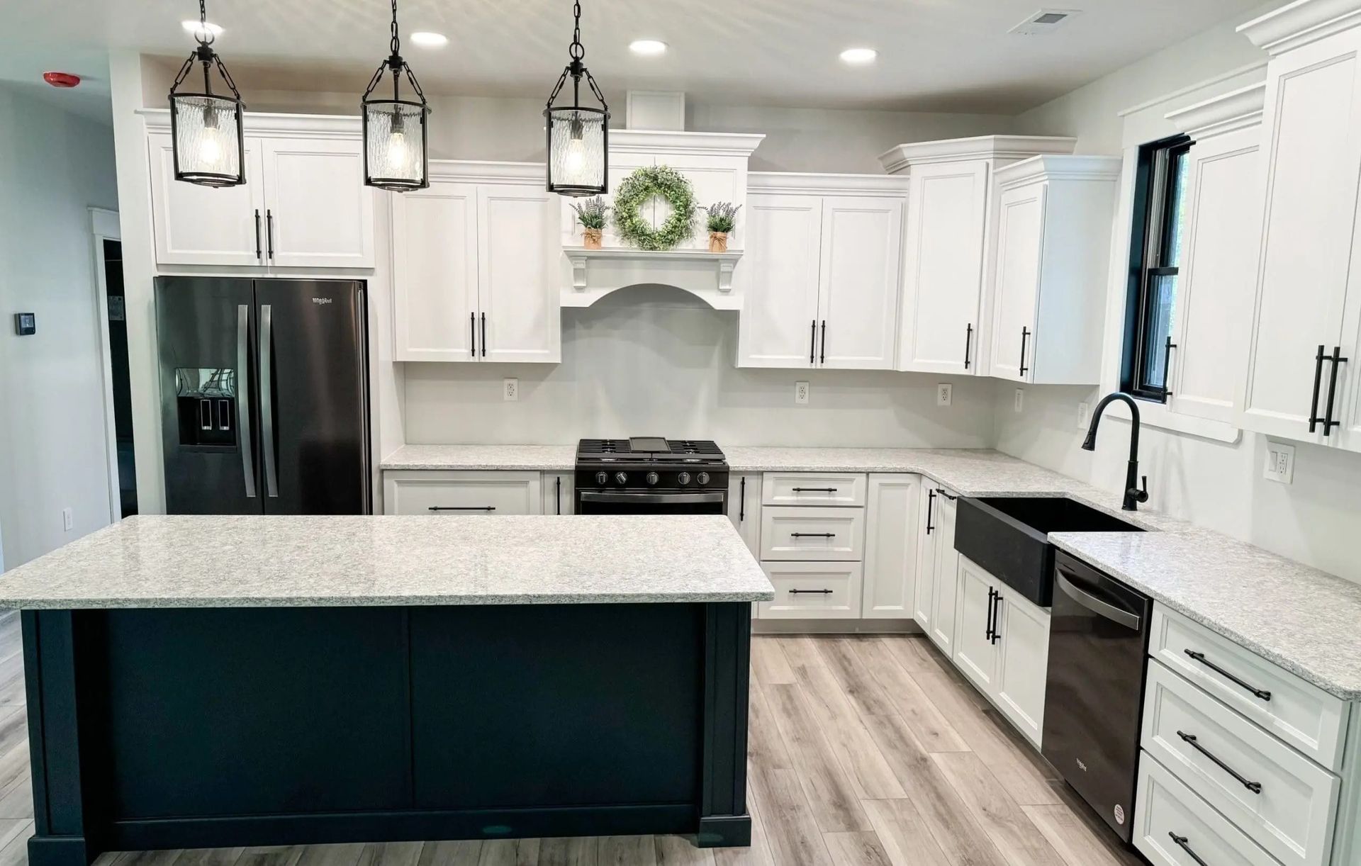 A kitchen with white cabinets , black appliances , granite counter tops , and a large island.