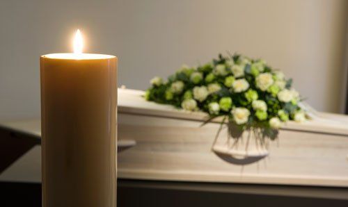una candela accesa e di fronte una bara con dei fiori sopra