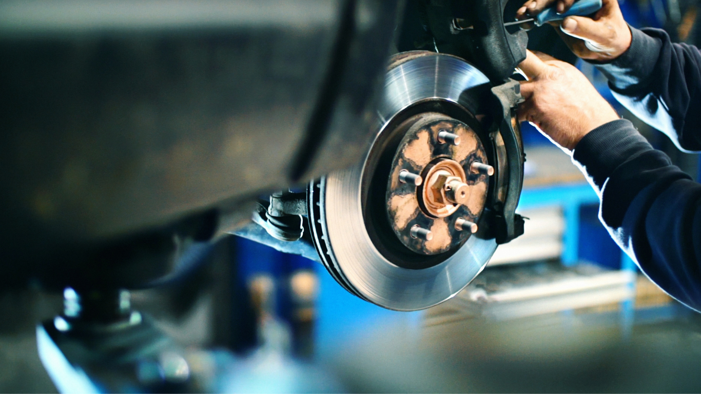 Mechanic working on car's brake disc and caliper in a garage setting.