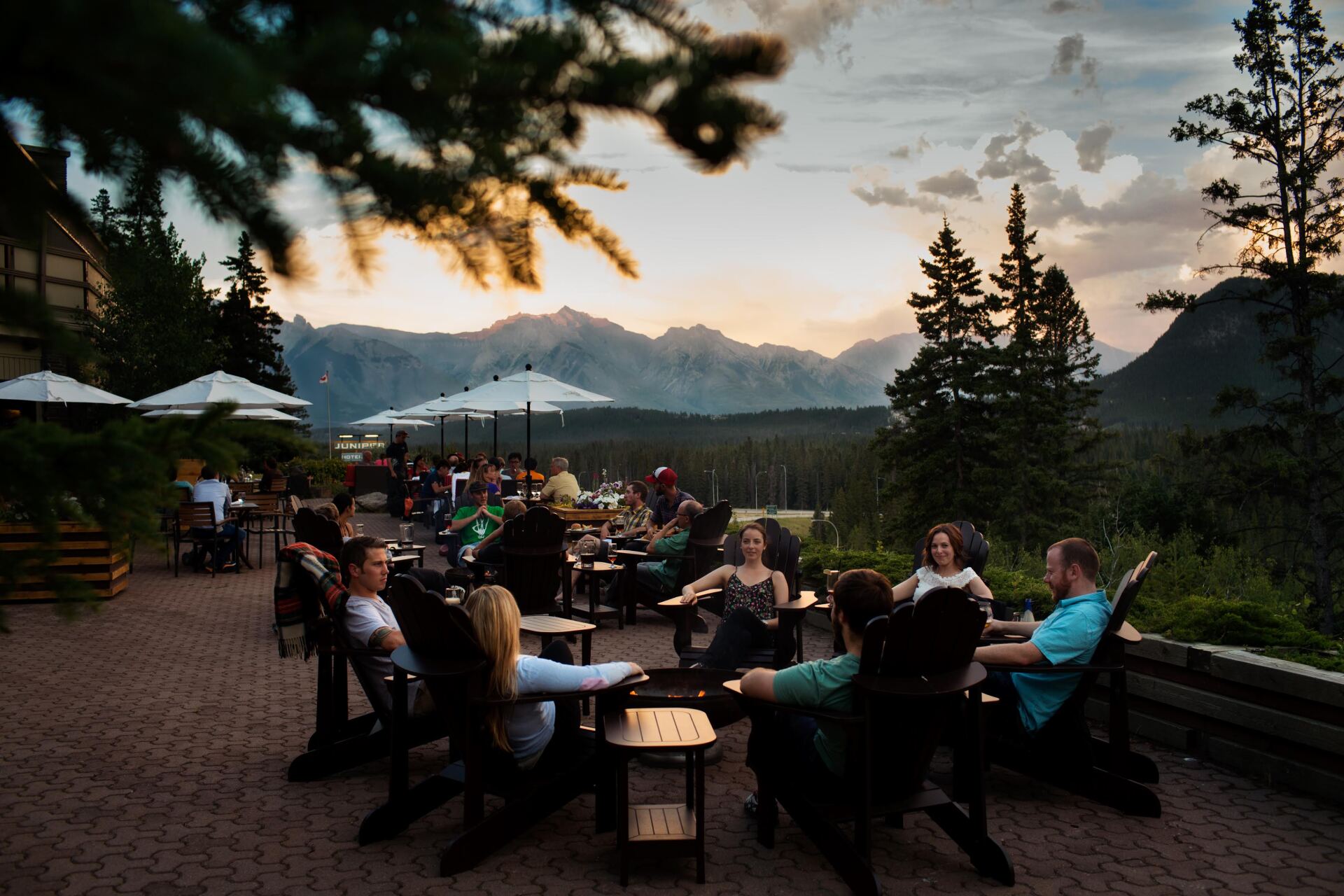 A group of people are sitting at tables outside with mountains in the background.