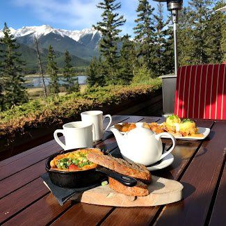 A wooden table topped with food and a teapot with mountains in the background.