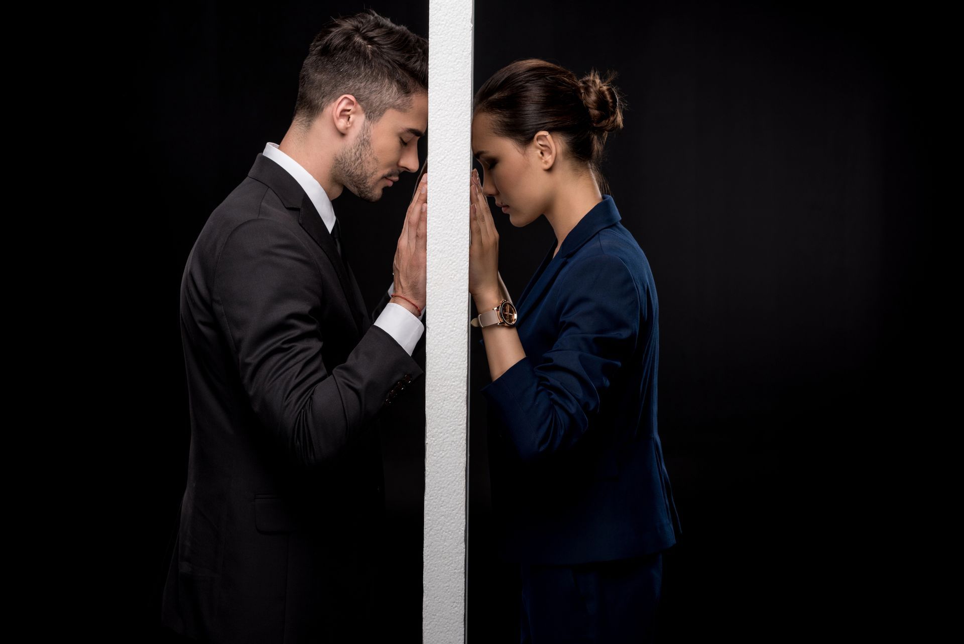 A man and a woman are standing next to each other with a wall between them.