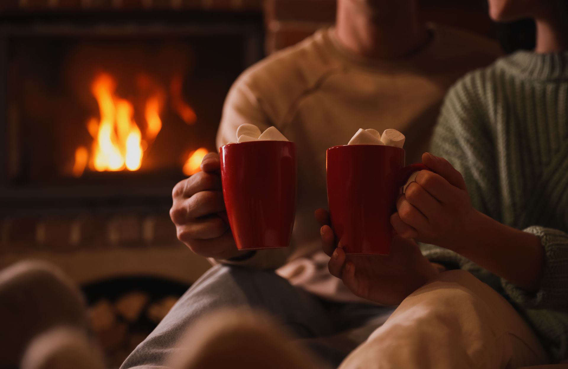 Two people holding red mugs with marshmallows in front of a fireplace.