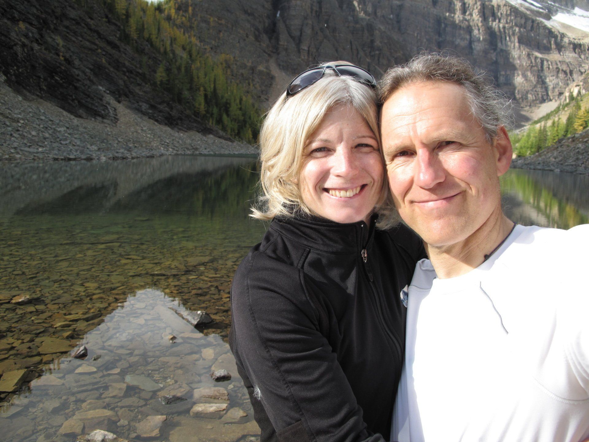 A man and a woman are posing for a picture in front of a lake.