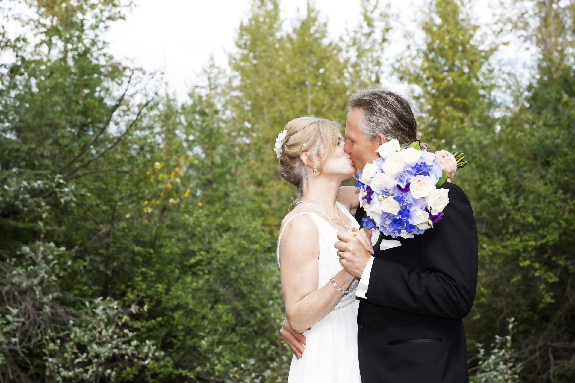 A bride and groom kissing while holding a bouquet of flowers.