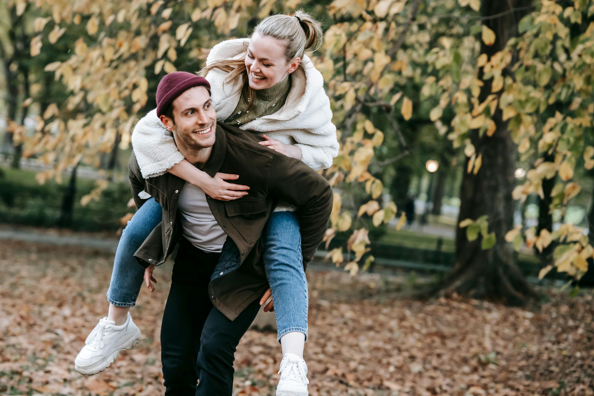 A man is carrying a woman on his back in a park.