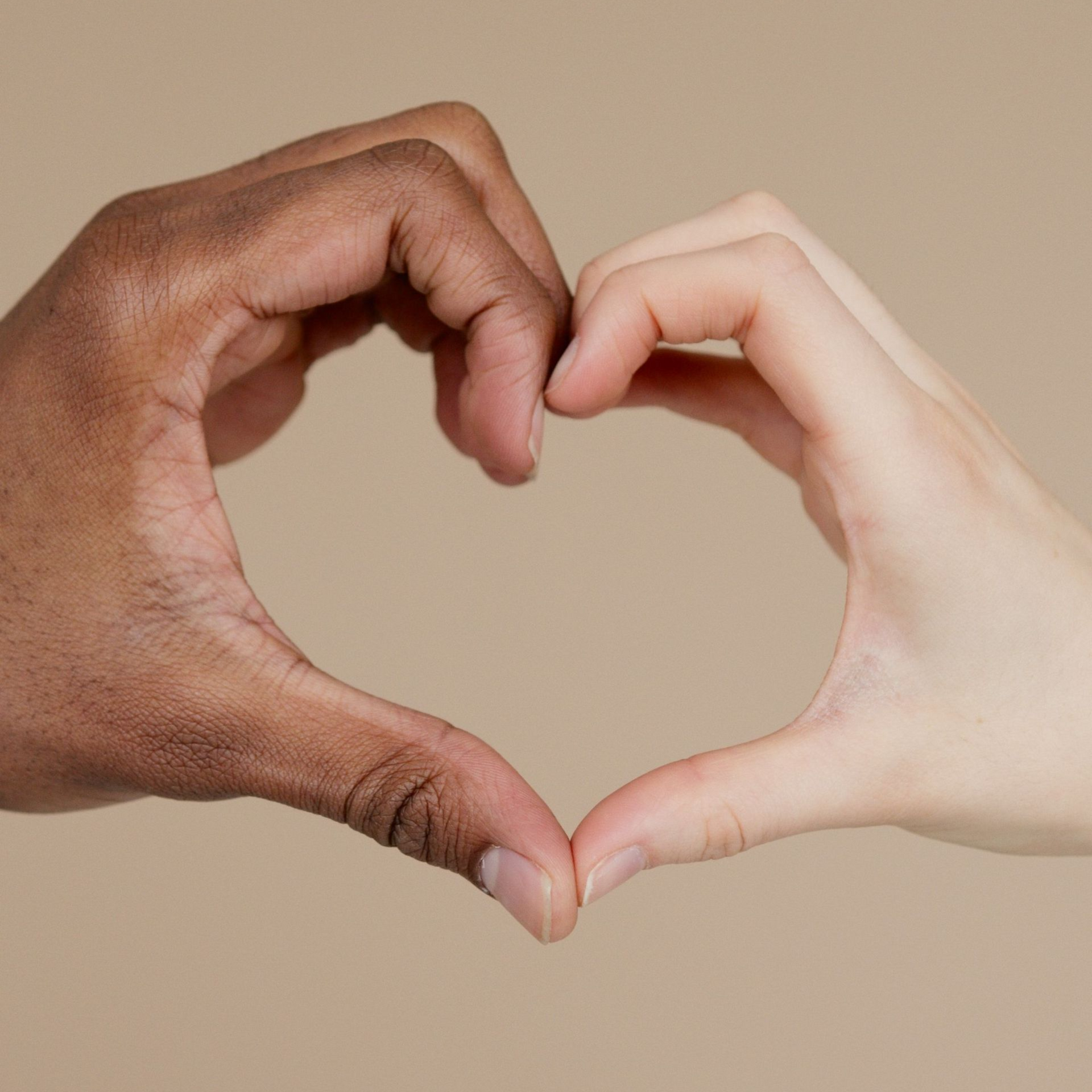 Two hands, one dark and one light, forming a heart shape against a beige background