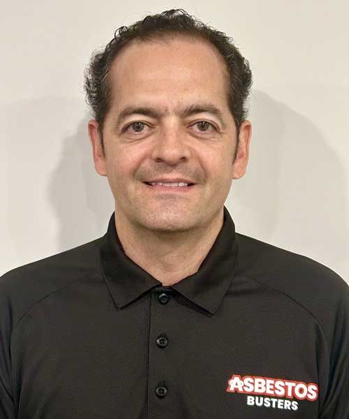 A man wearing a black asbestos busters shirt is smiling for the camera.