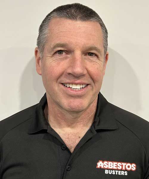 A man wearing a black shirt that says asbestos busters is smiling for the camera.
