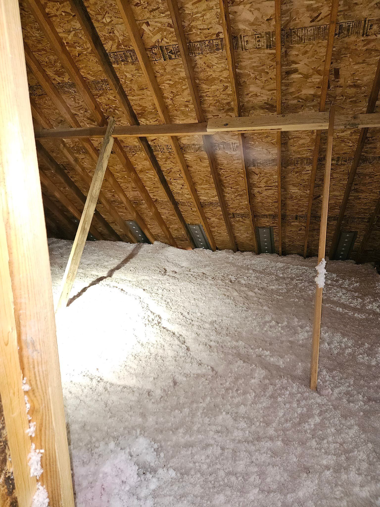 Attic with loose-fill insulation, wood beams, and a bright light source visible.