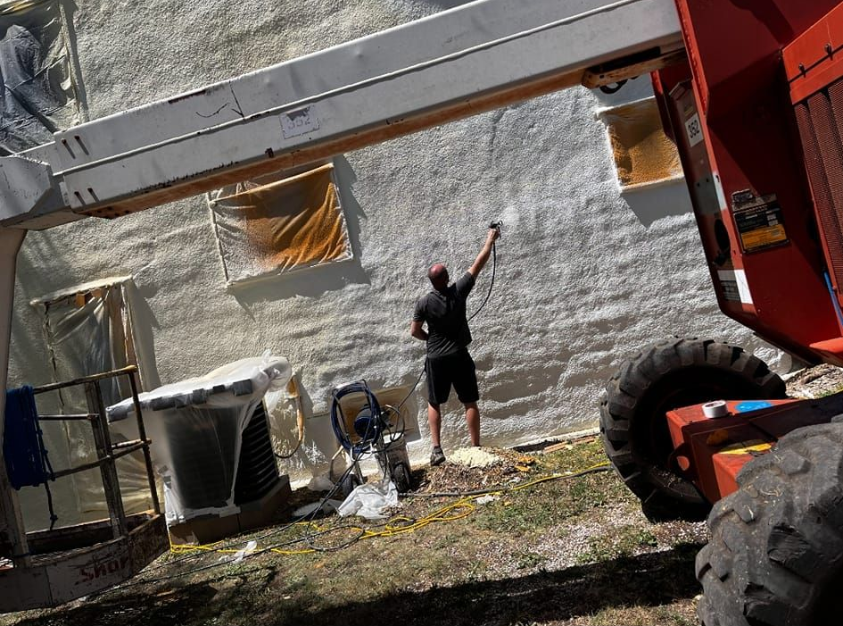 Man in black shorts points at a building as machinery lifts a metal beam. Outdoors.