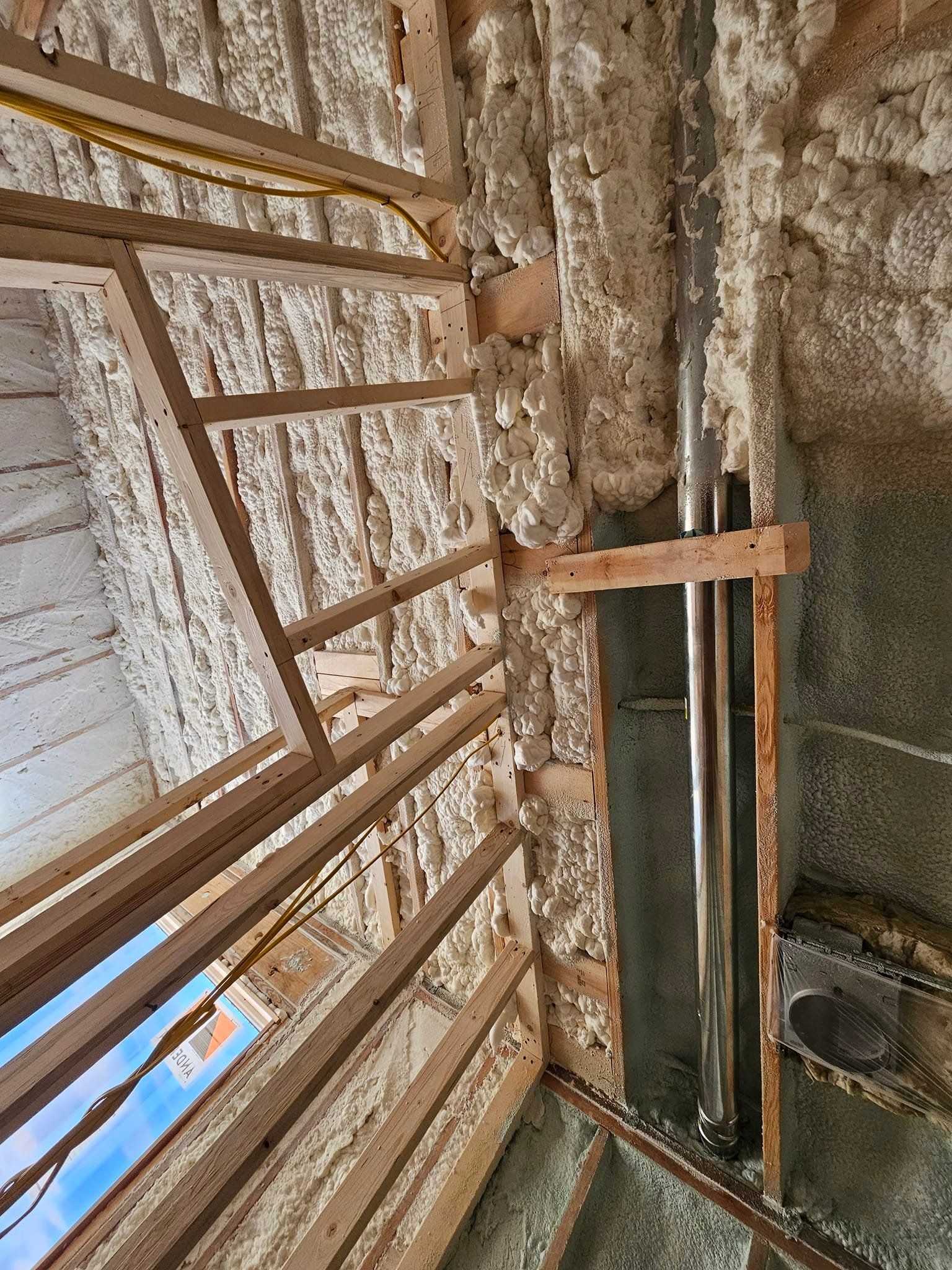 Interior framing with spray foam insulation, a chimney, and a partially framed window.