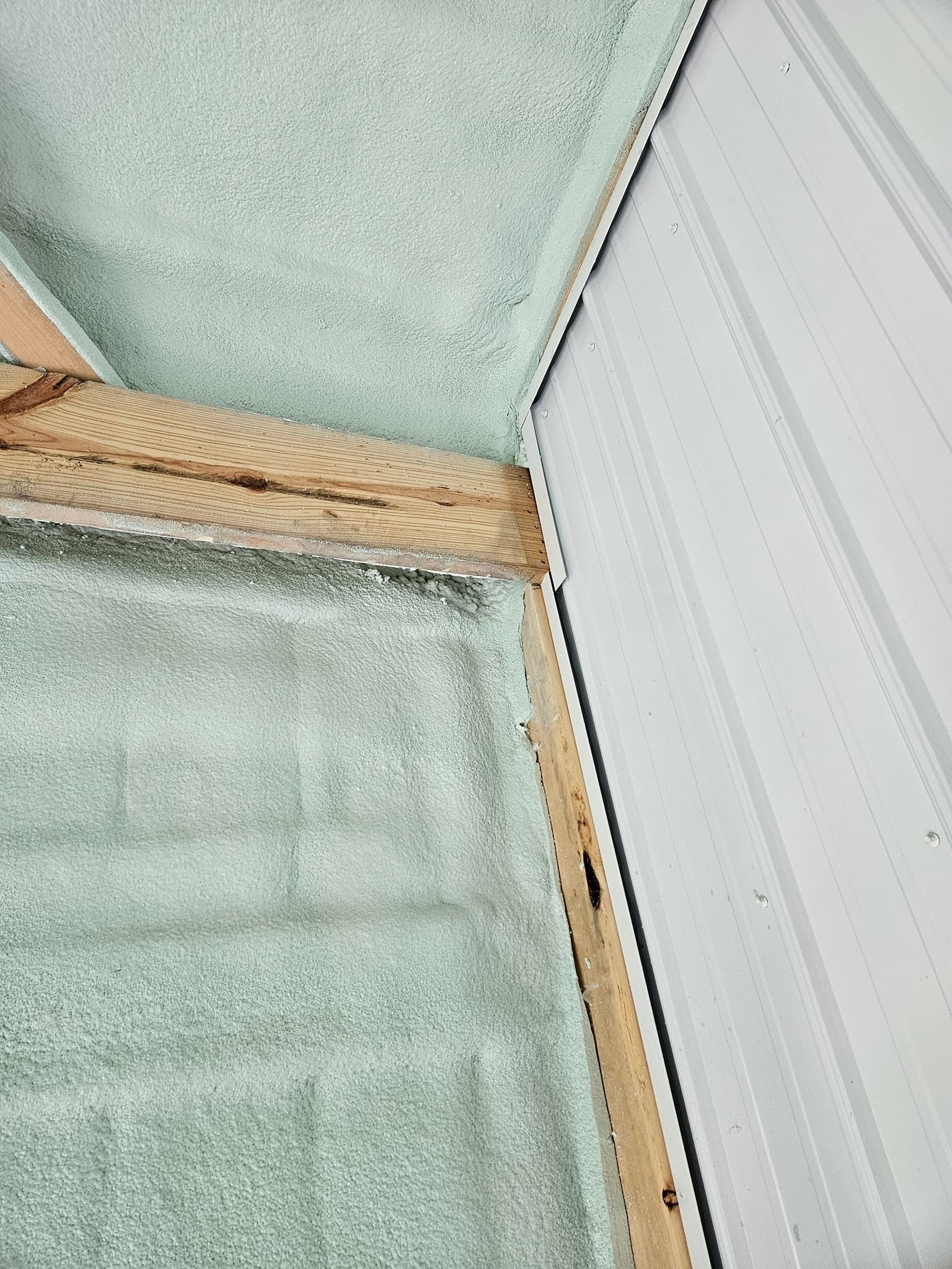 Metal roofing and wooden beams meeting. Green insulation present.