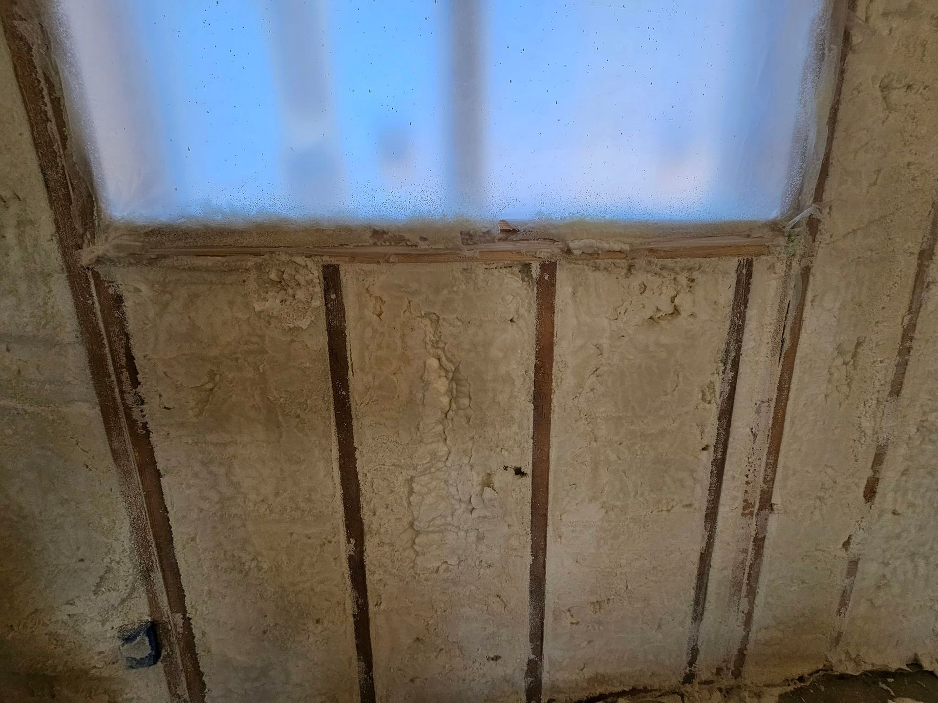 Interior view of a weathered wall with a frosted window. Vertical wood strips separate textured, beige panels.