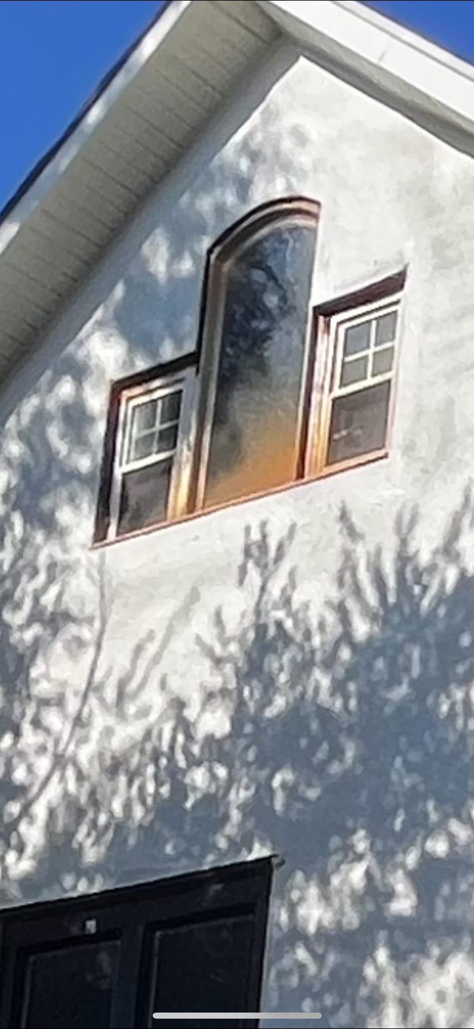 White building with unusual windows; a large, curved window is between two smaller, rectangular windows.