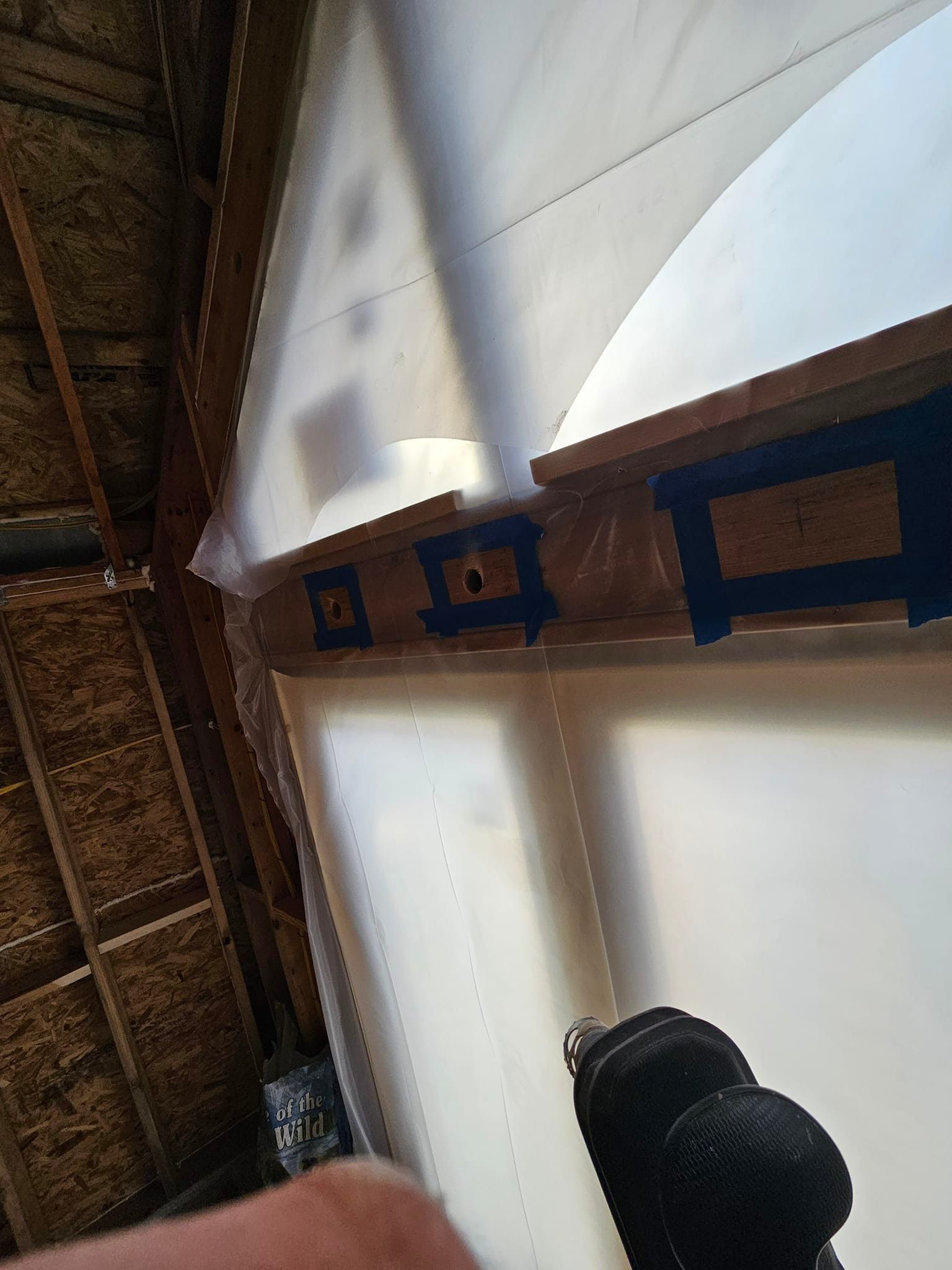 Drill pointed at a wooden frame, secured with blue tape. White covering on frame; interior setting.