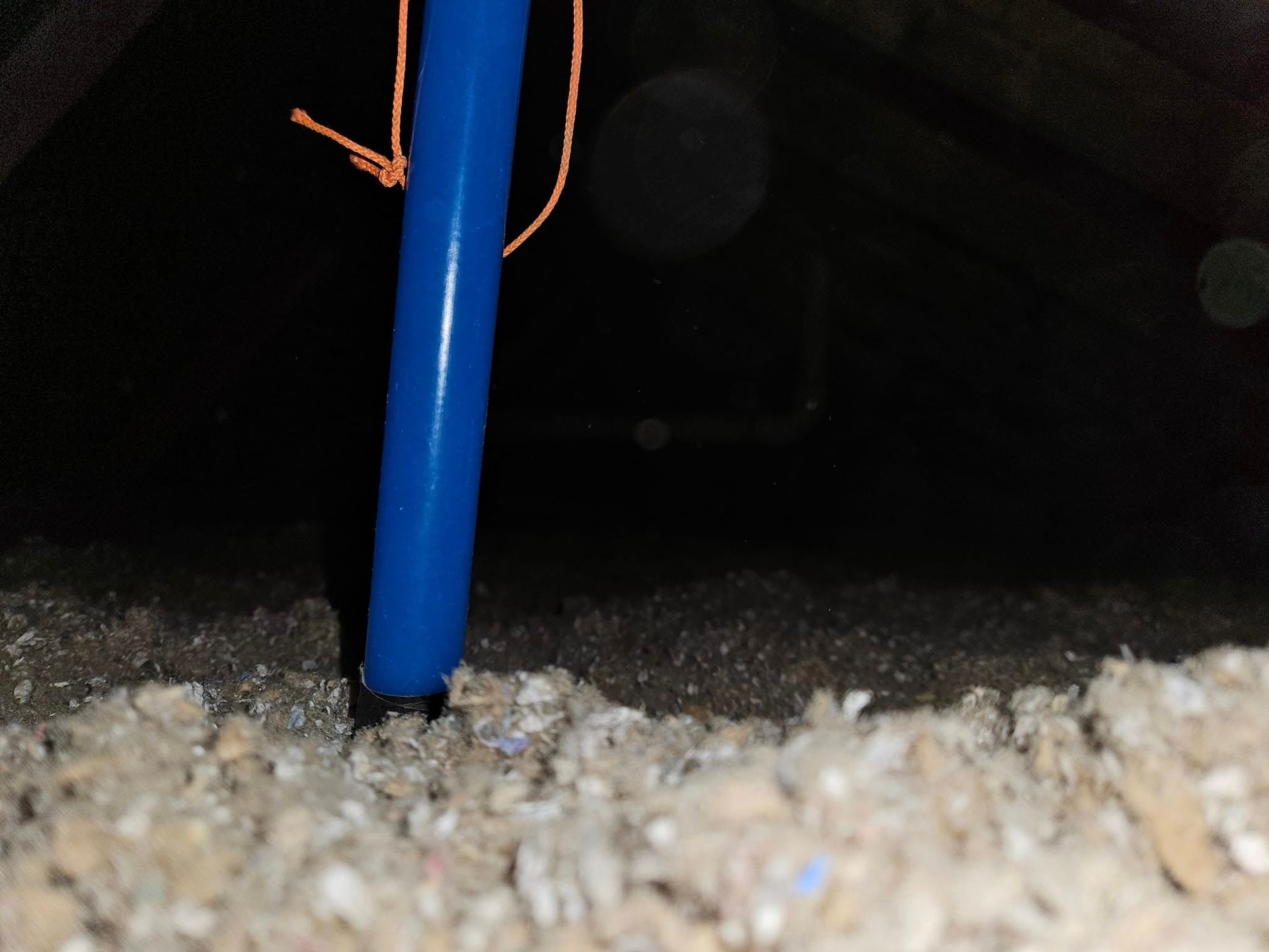 Blue pipe in an attic, penetrating insulation, with a dark background.
