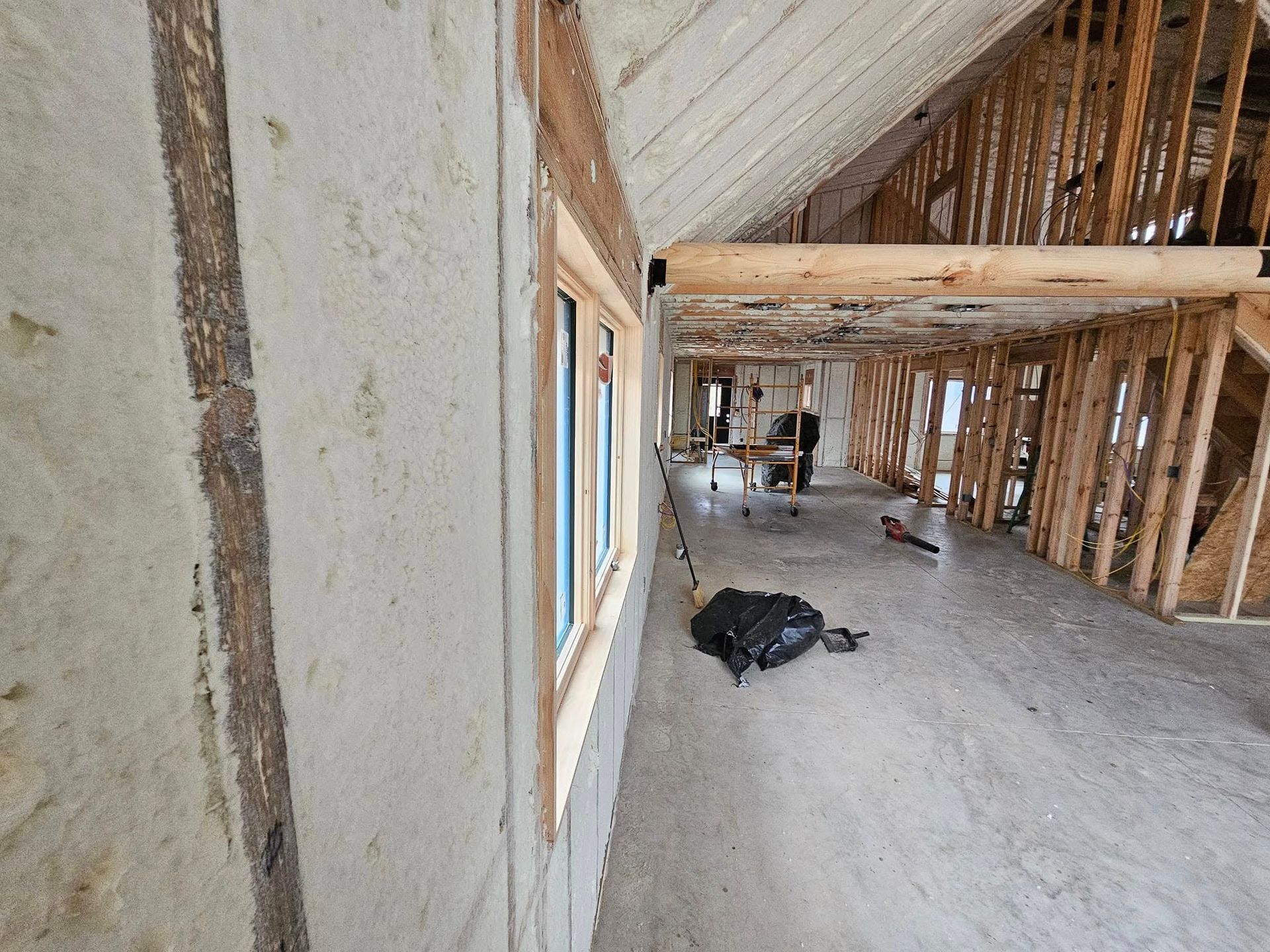 Interior of a building under construction, showing framing, insulation, a window, and exposed beams.