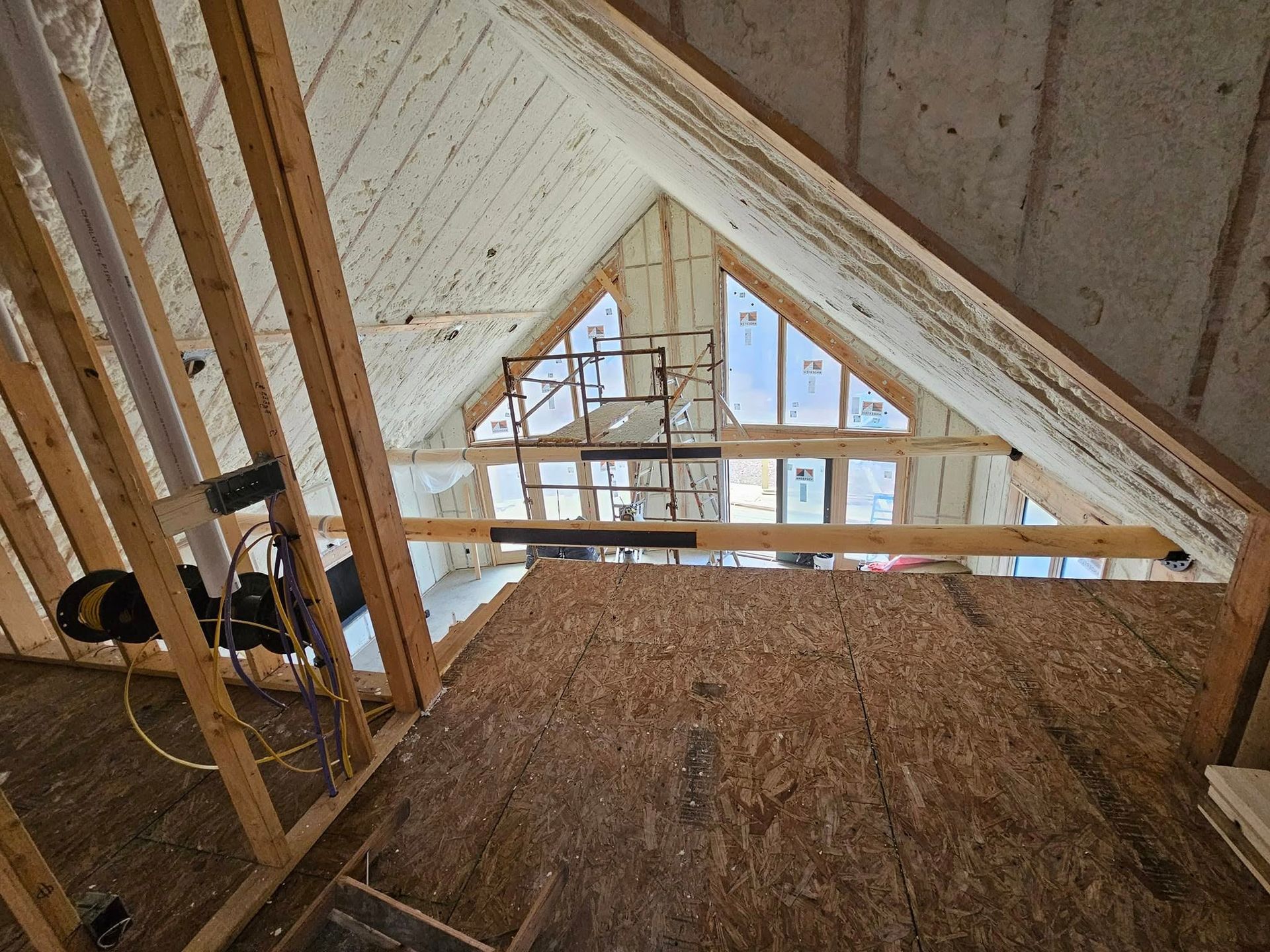Interior view of an attic with spray foam insulation on the rafters and a partially built floor.