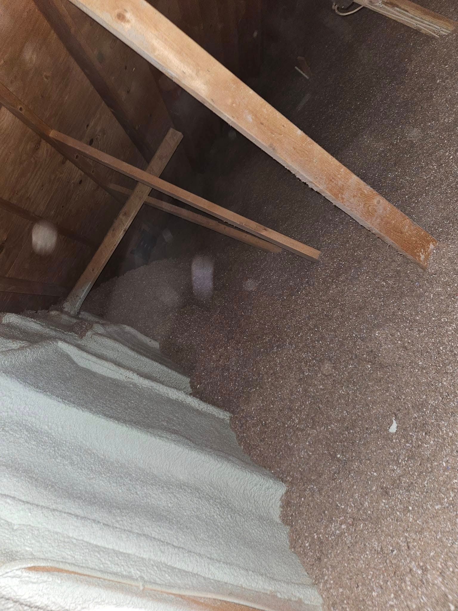 Attic interior with brown and white insulation between wooden beams.