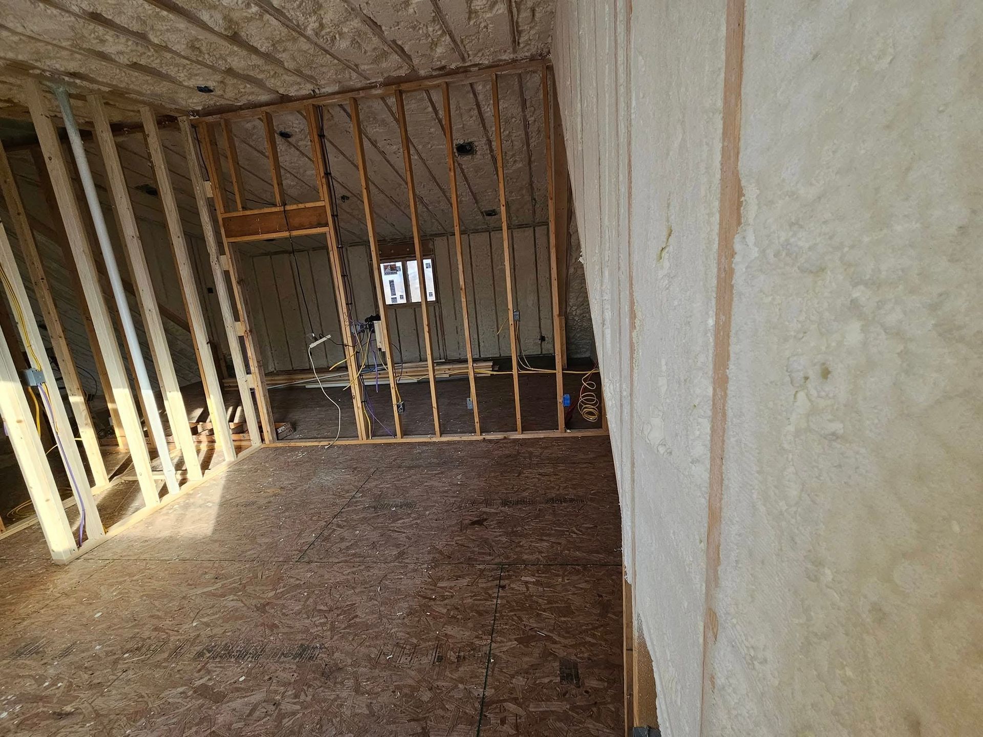 Interior view of a room under construction, showing wooden framing, insulation, and unfinished walls and flooring.