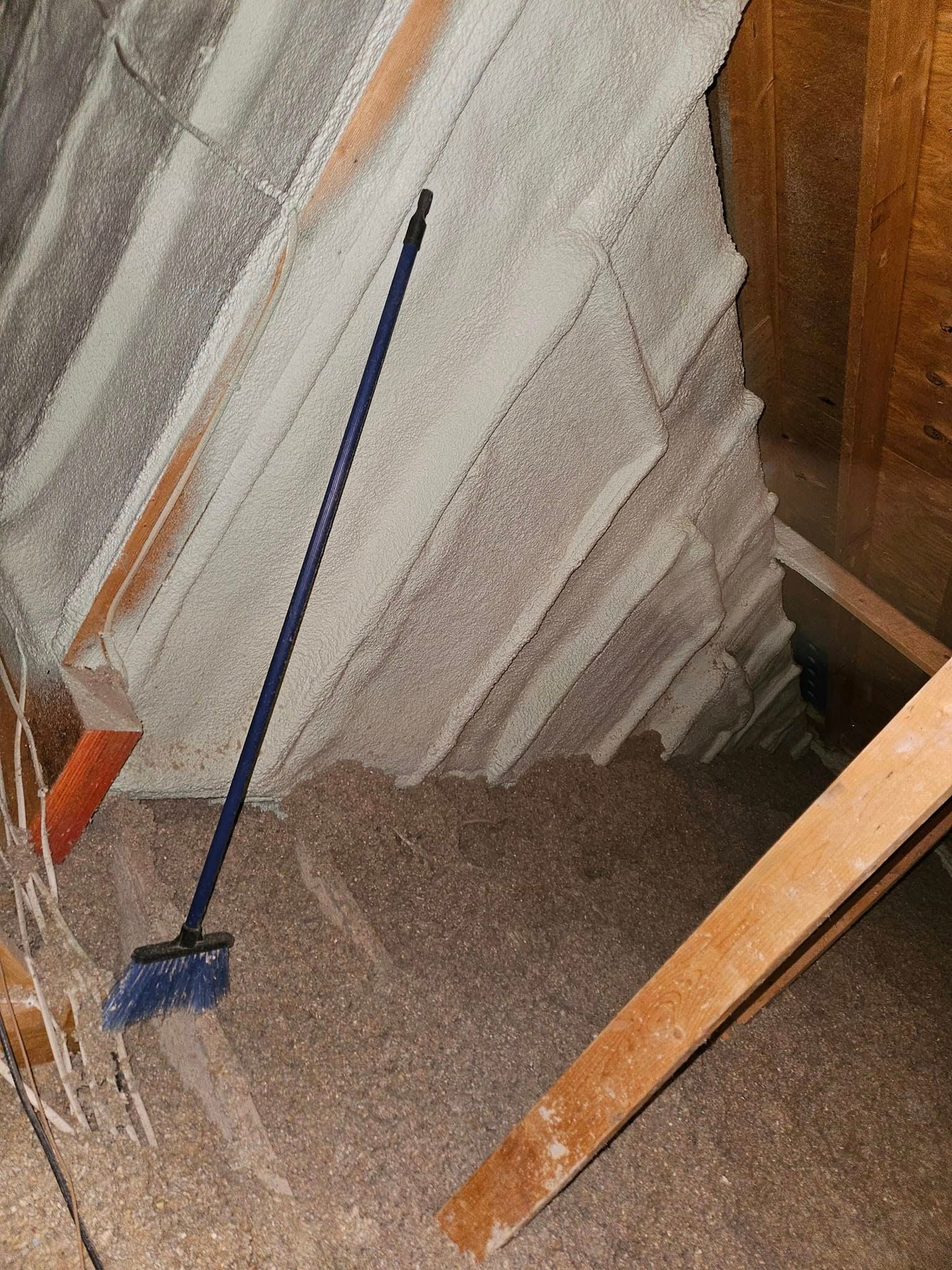 Attic space with thick insulation, a blue broom, and wooden supports.