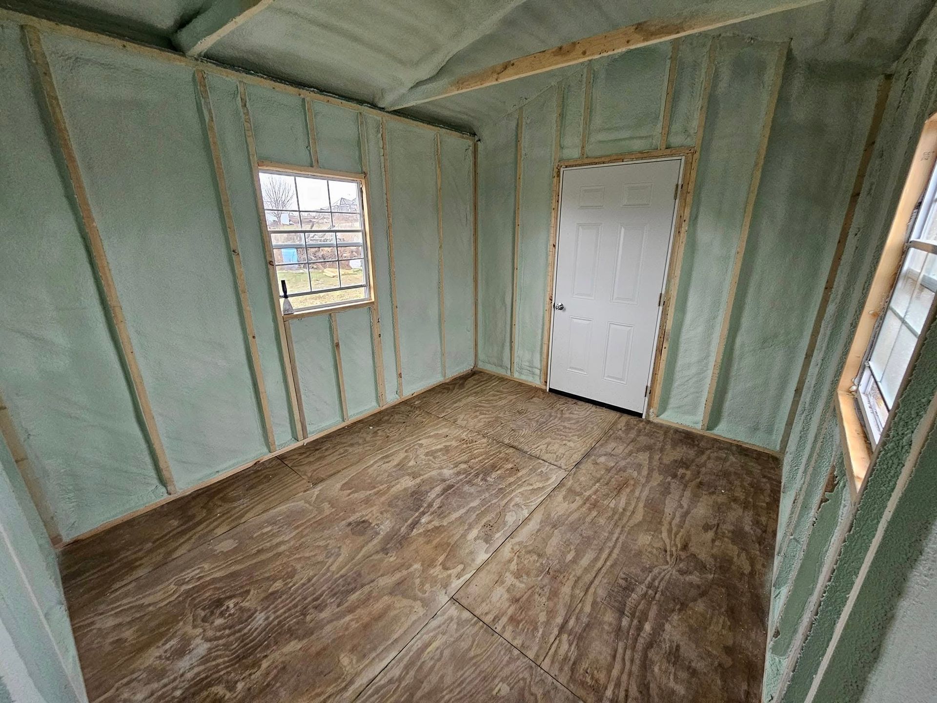 Interior of a shed with wood flooring, insulated walls, door, and windows.