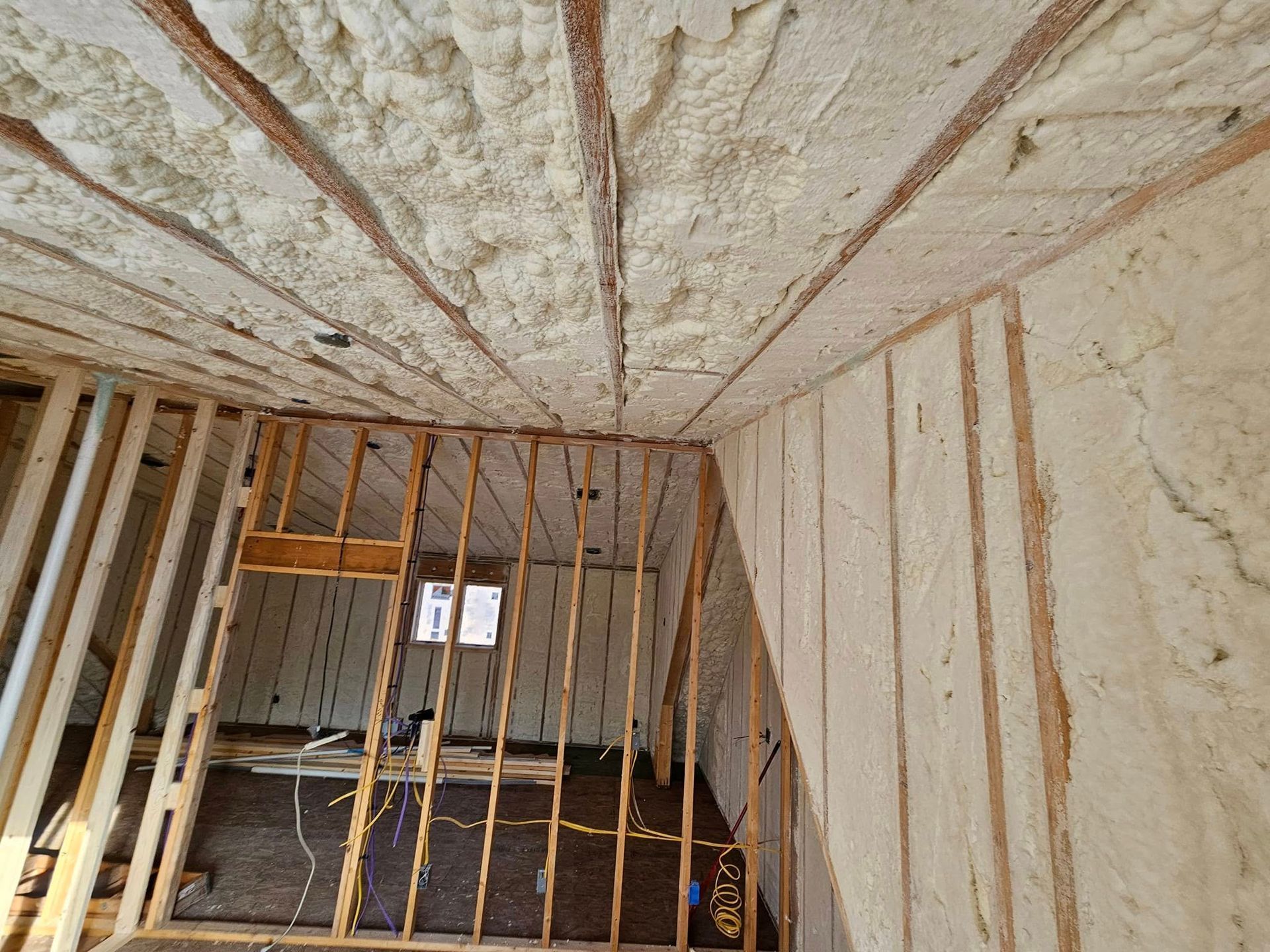 Interior view of an attic with spray foam insulation on the walls and ceiling, framing visible.