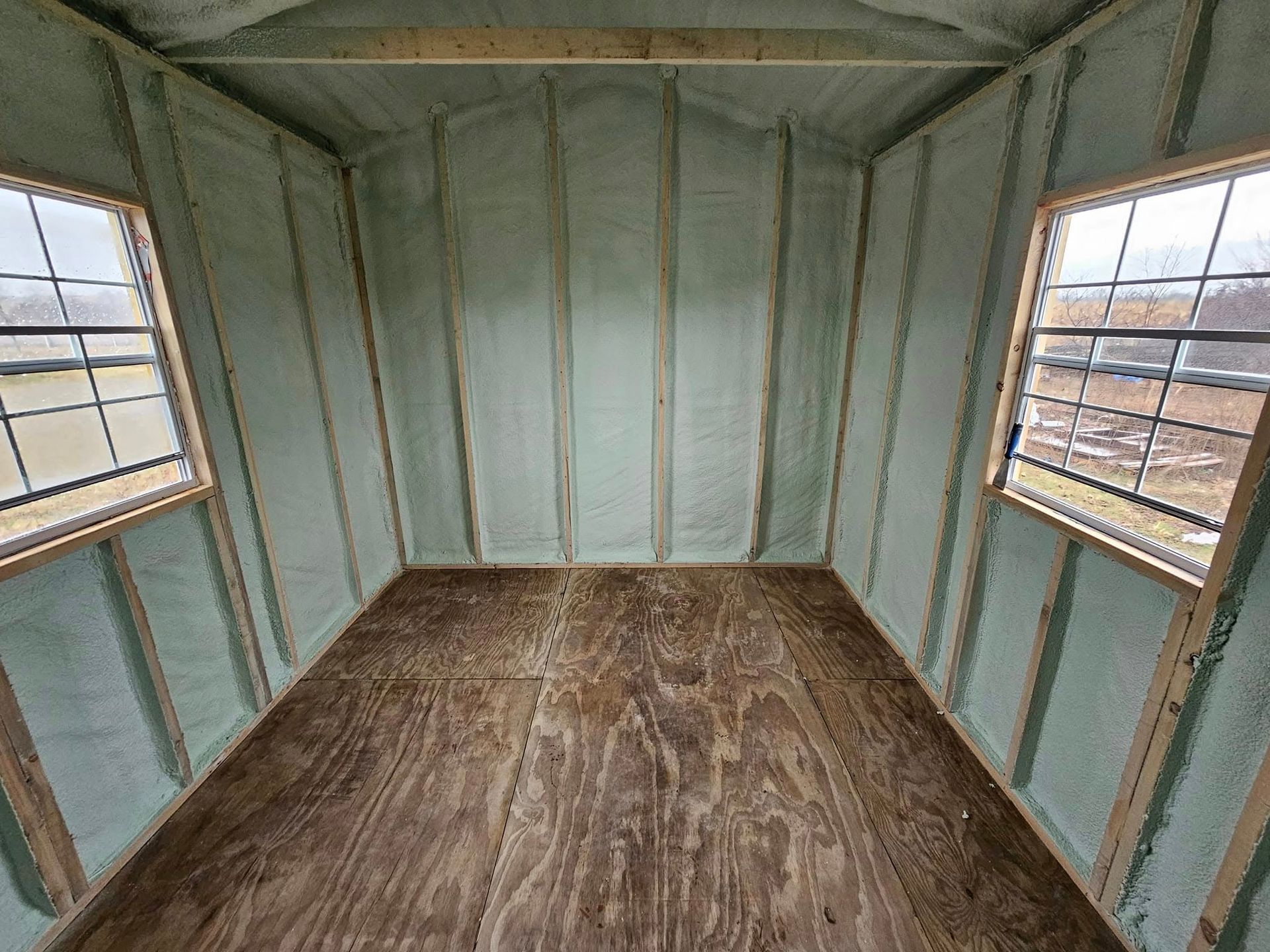 Inside of a shed with spray foam insulation on the walls and two windows.
