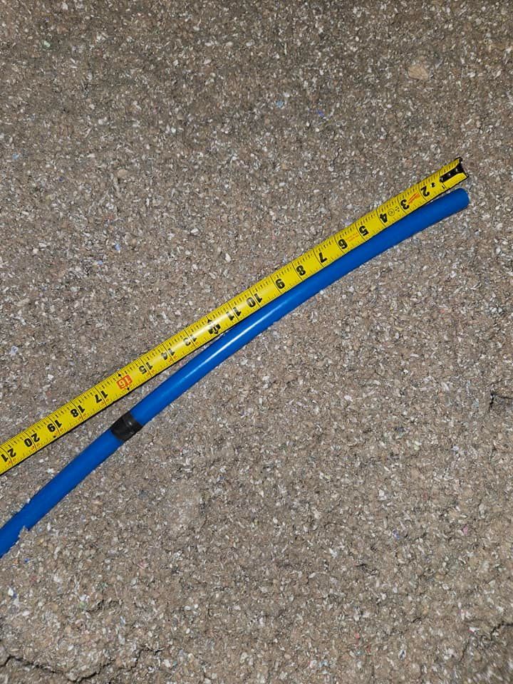 Blue plastic tubing next to a yellow measuring tape on a gray concrete surface.