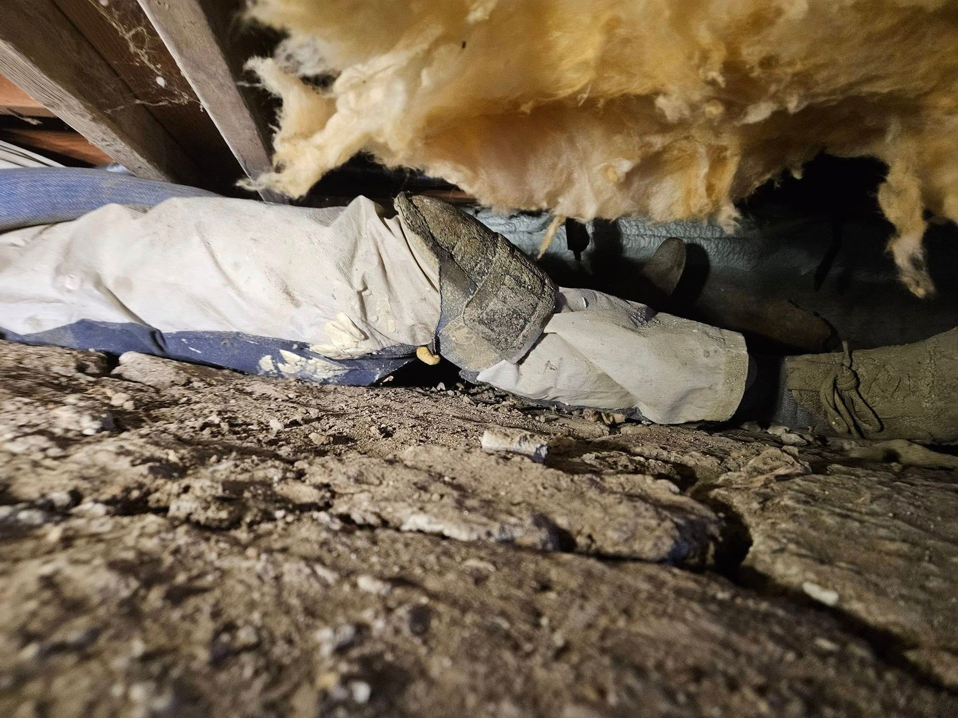 A pile of debris, possibly insulation and concrete, against a dark background in an attic.