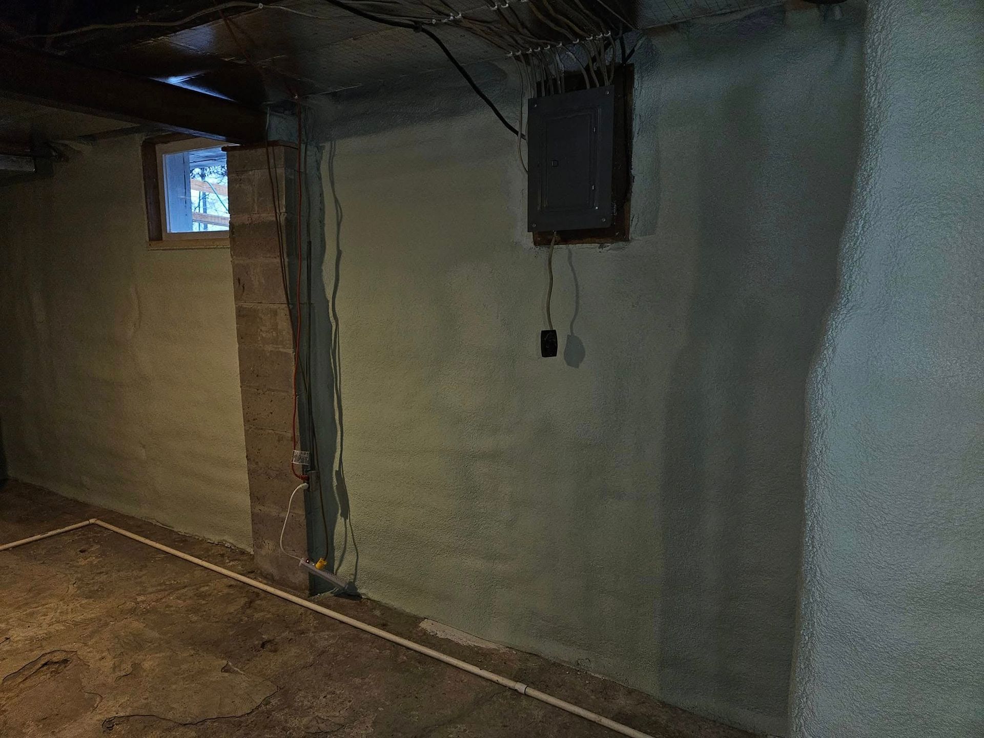 Basement interior with gray walls, electrical panel, window, and concrete floor.