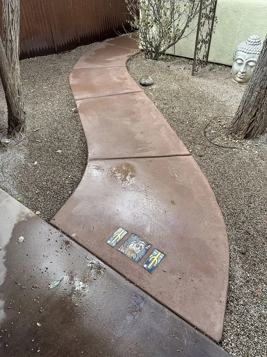 Curving, brown concrete walkway through a gravel yard, with trees and a Buddha head statue.