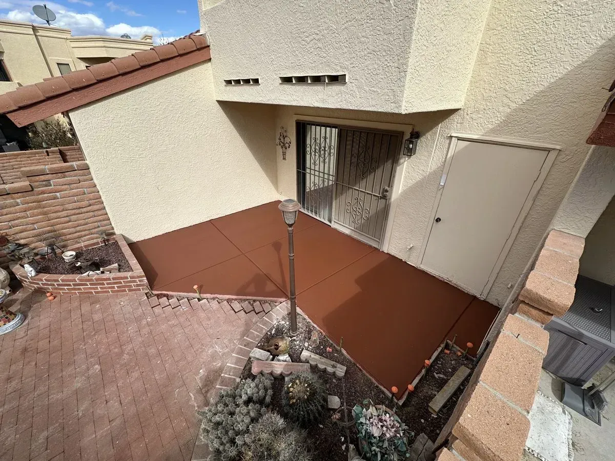 Exterior view of a beige building with a brown deck, door, and a brick pathway.
