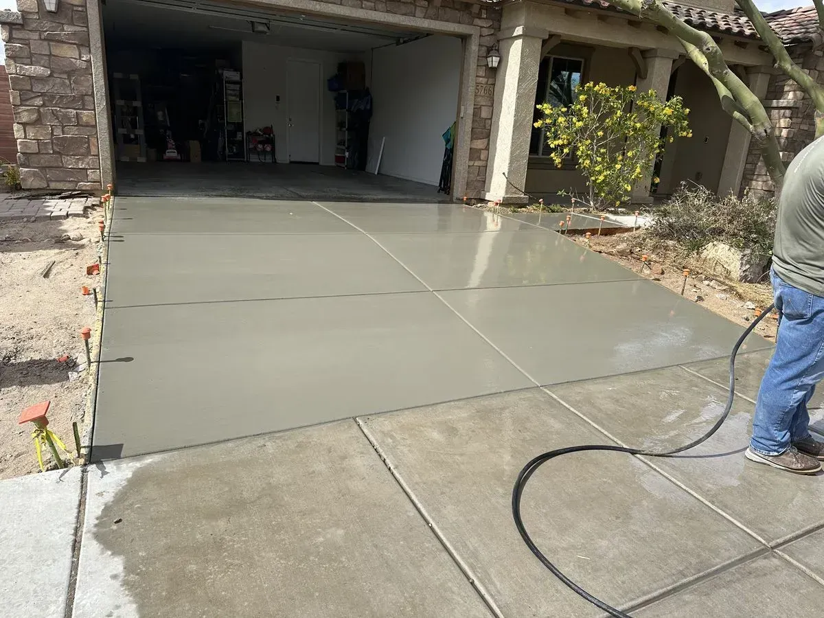 Freshly poured concrete driveway in front of a house. Person spraying water.