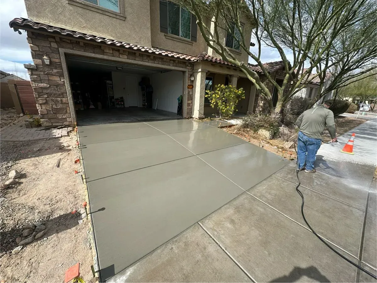 Newly poured concrete driveway in front of a house; a person sprays the surface.