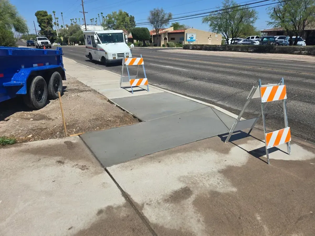 New concrete sidewalk with orange and white barricades. A mail truck is nearby.