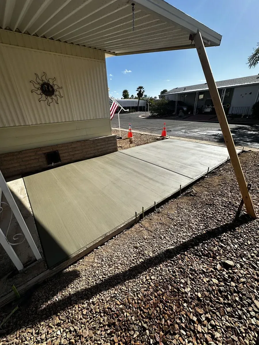 New concrete patio adjacent to a light-colored mobile home, with gravel and a wooden support beam.