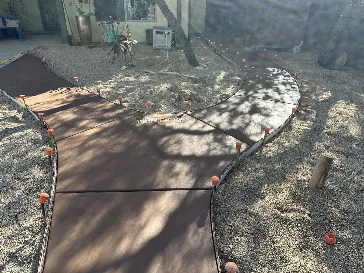 A curved concrete walkway in a gravel yard, edged with small orange markers and surrounded by light gravel.