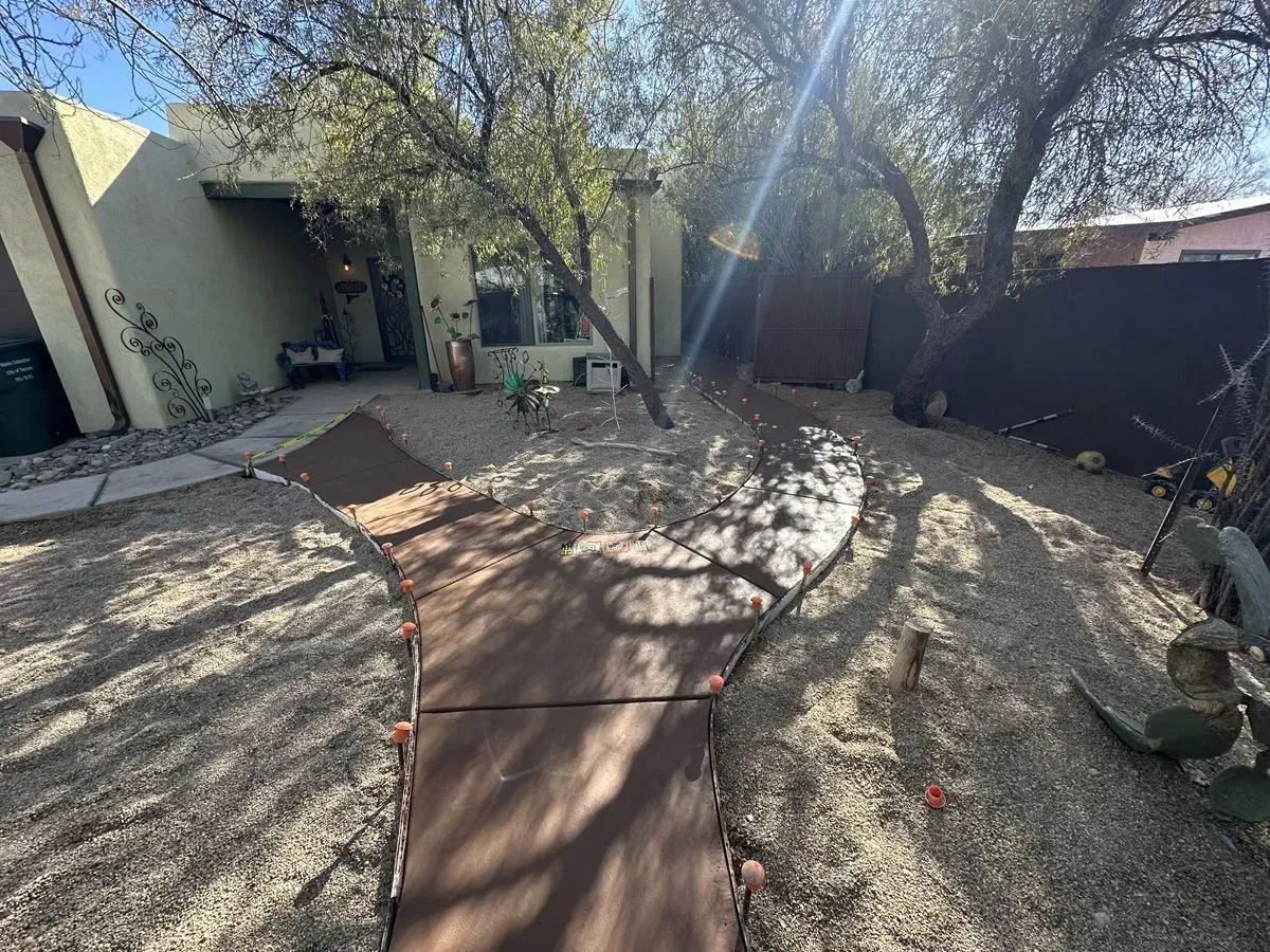 Pathway leading to a light-colored building with desert landscaping and trees; sunny outdoor setting.