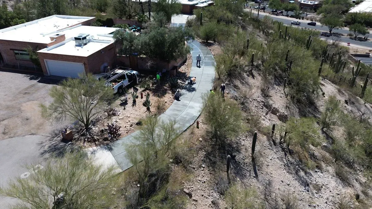Aerial view of a concrete path being constructed on a hillside, with a building on the left.