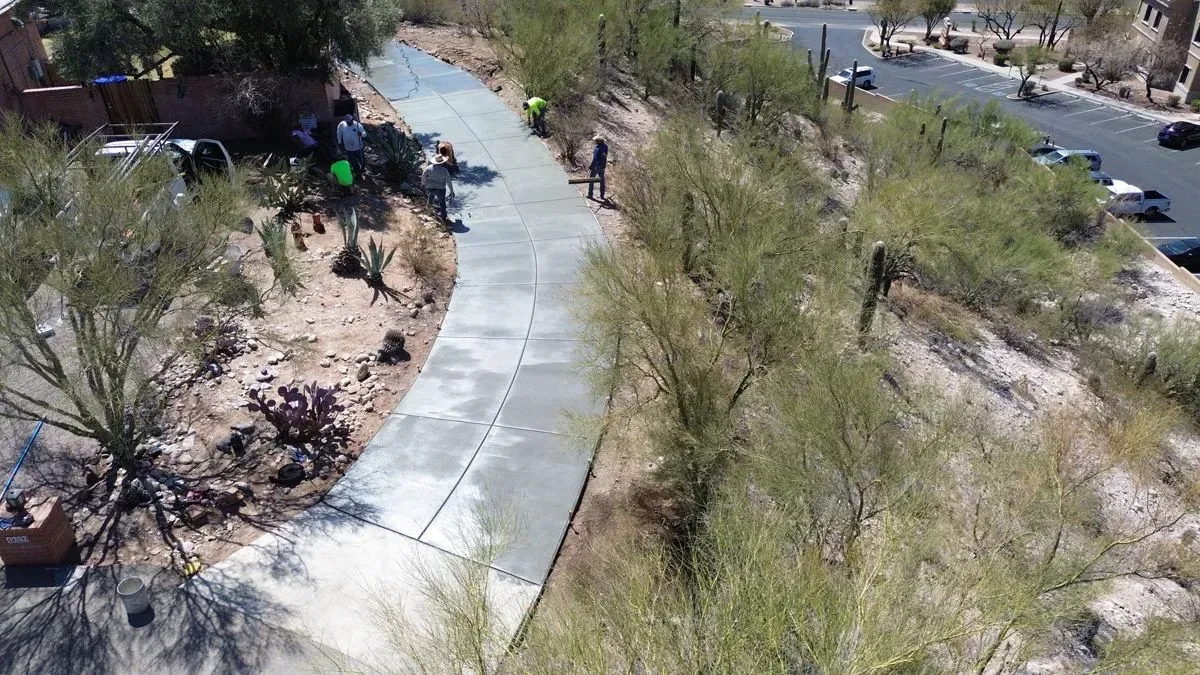 Workers constructing a concrete path on a hillside, surrounded by desert vegetation.