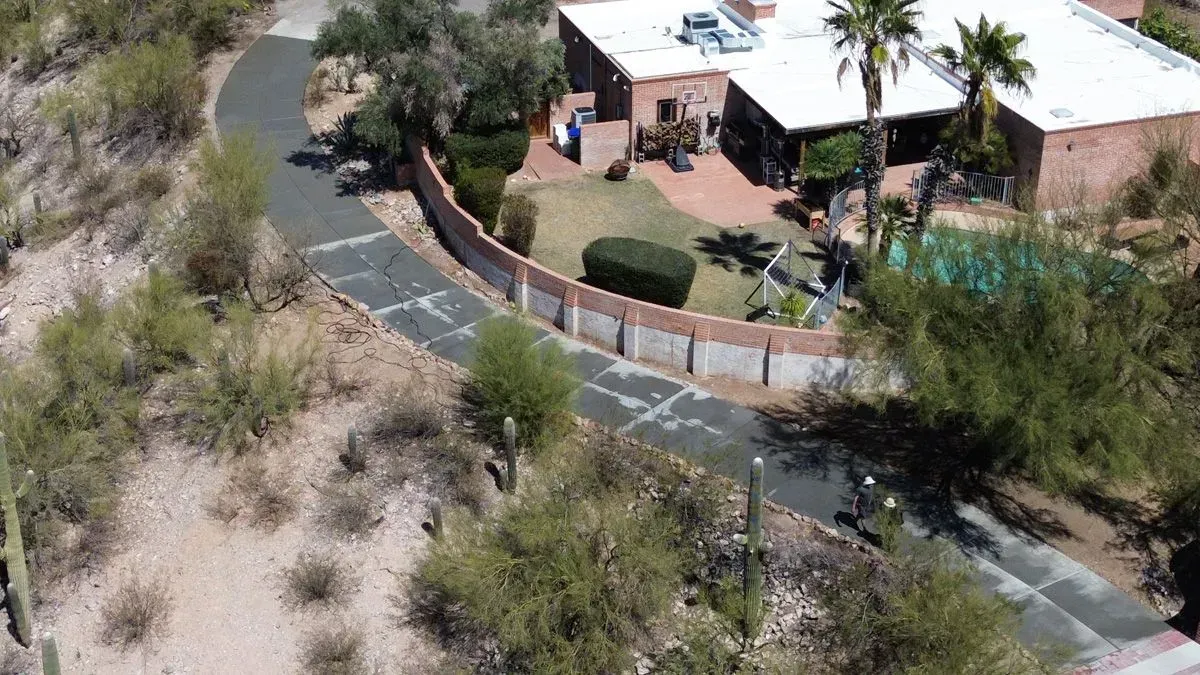 View of a house with a curved driveway, surrounded by desert vegetation. The house has a pool.