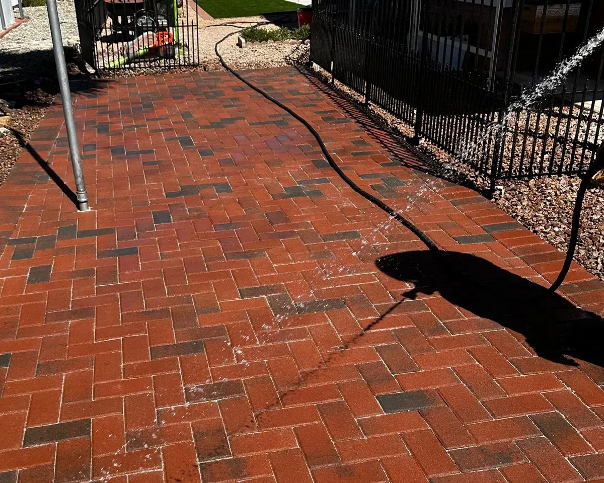 Brick patio being hosed down, water spraying across the red and brown bricks.