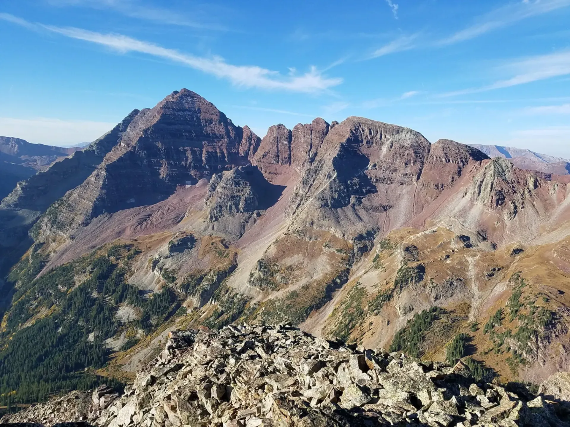 A high-angle view of the dramatic, reddish-brown peaks of the Maroon Bells in Colorado under a bright blue sky.