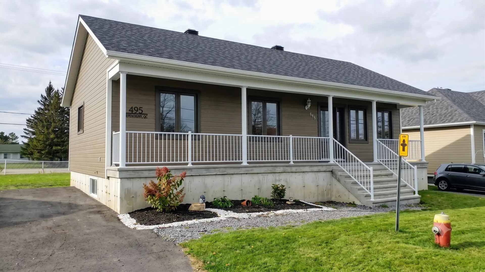 Maison beige de plain-pied avec porche, marches, pelouse et jardin paysager par une journée ensoleillée