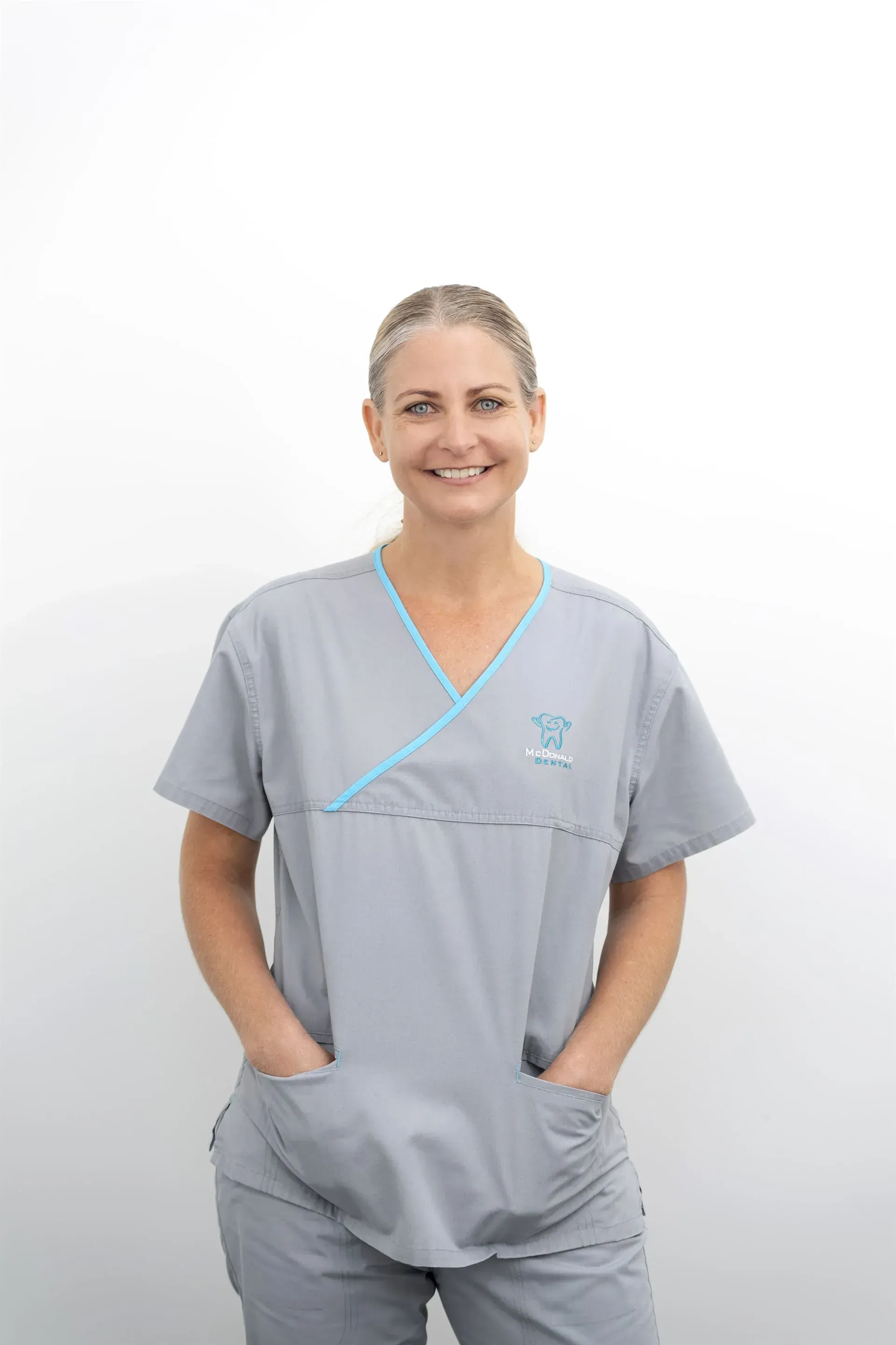 Woman in grey medical scrubs smiles with hands in pockets. — McDonald Dental in Gympie, QLD